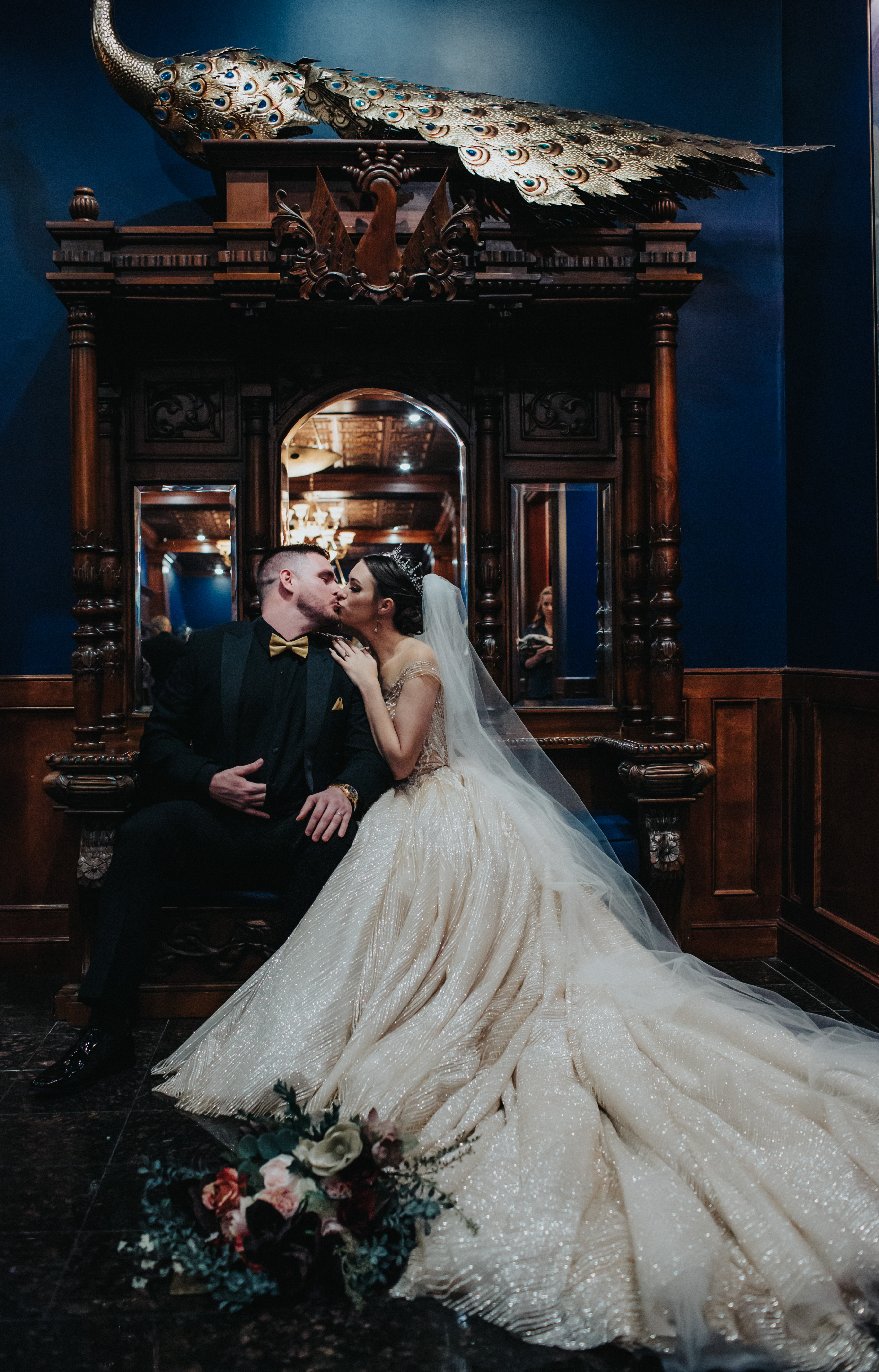 Caitlyn and her husband kissing beside a peacock sculpture