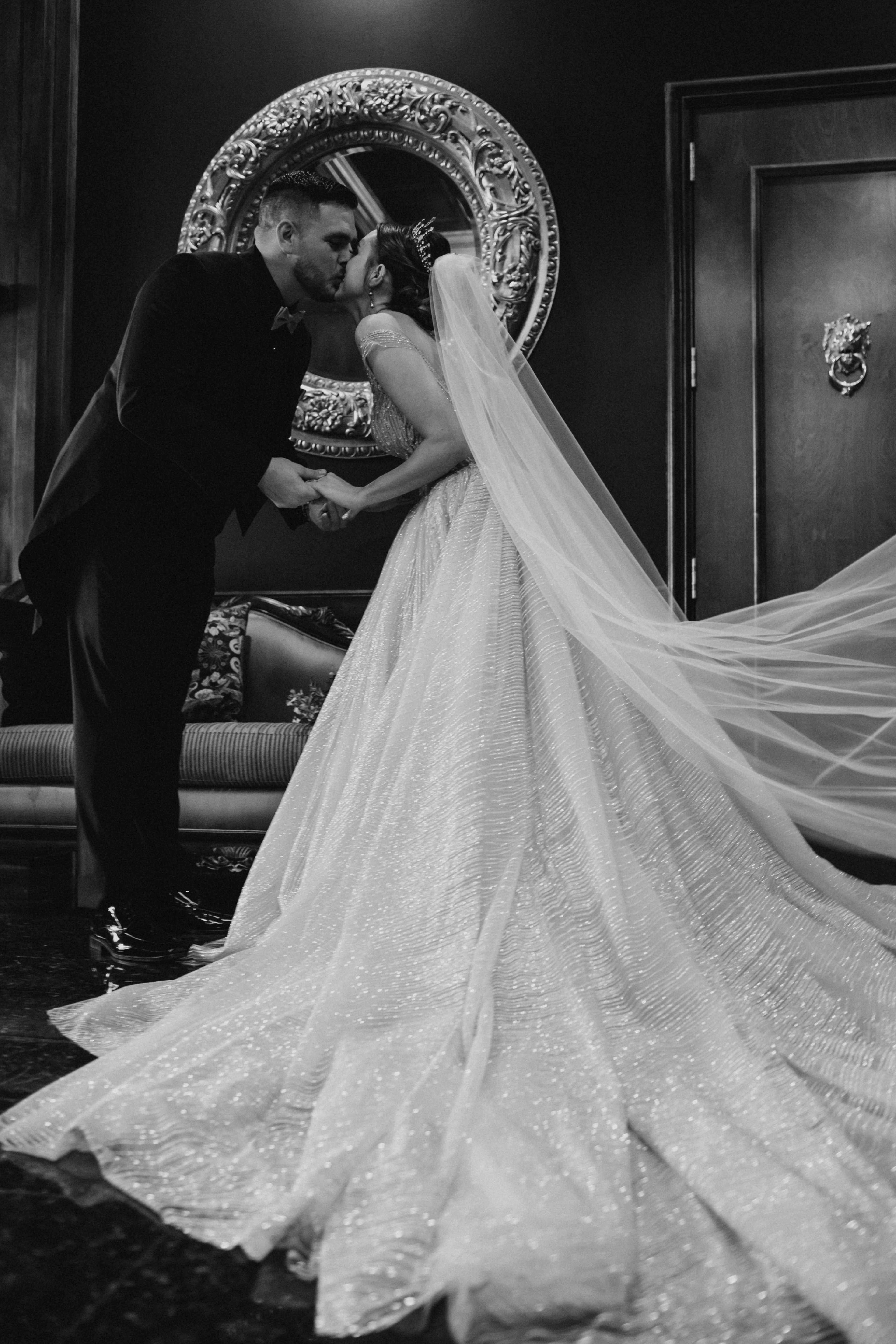 Couple kissing in front of an ornate gold mirror, veil flowing
